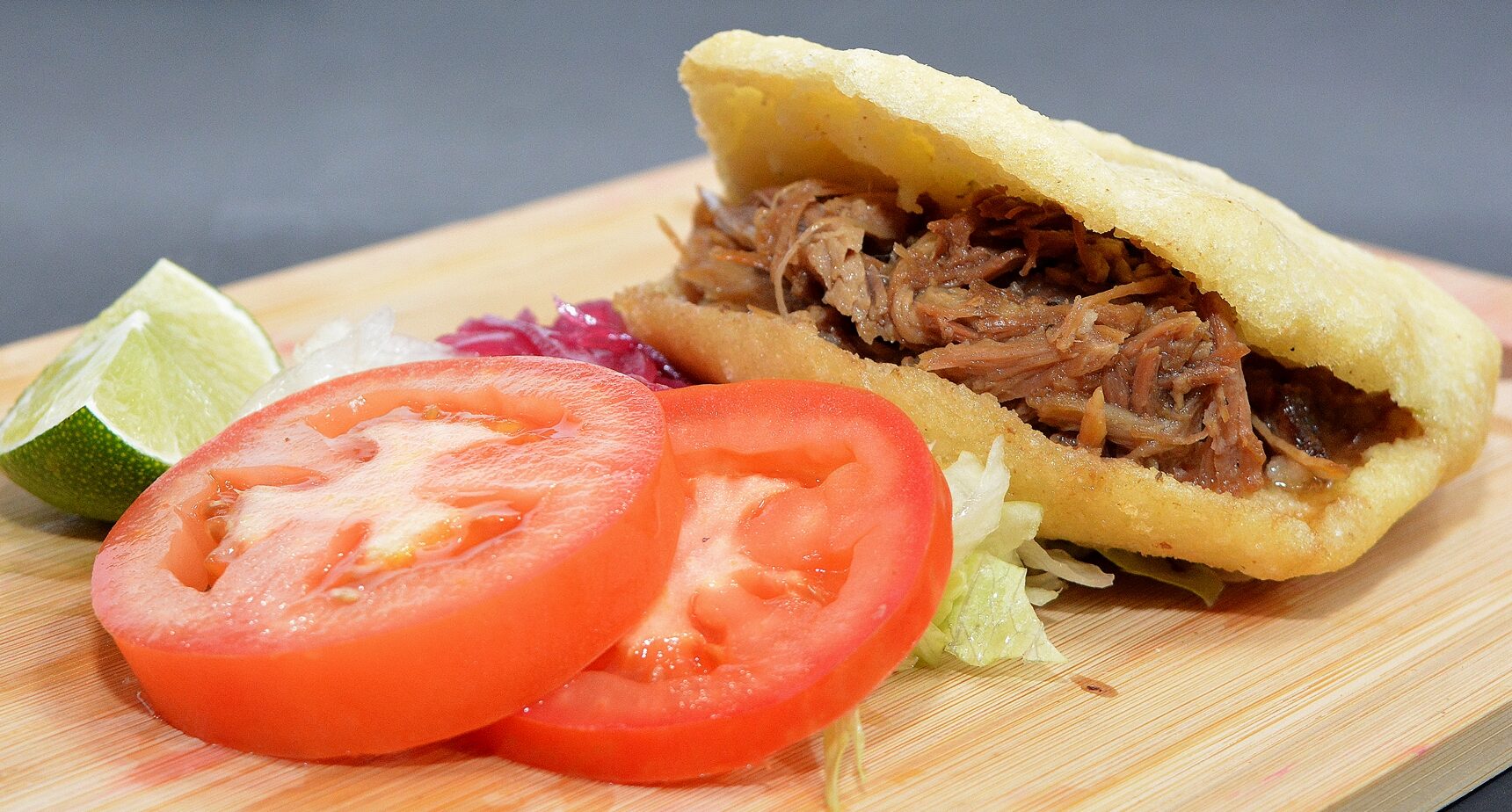 Colombian arepa de pernil filled with slow-roasted shredded pork, tomatoes, and lettuce